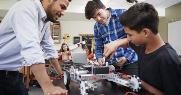 professor auxiliando dois alunos a construir um protótipo robótico