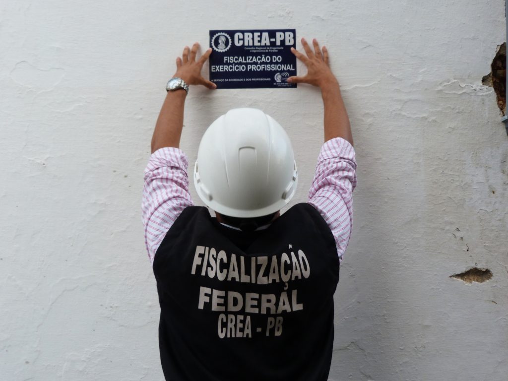 homem pregando placa de fiscalização do CREA em muro de obra