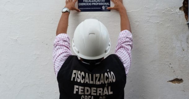 homem pregando placa de fiscalização do CREA em muro de obra