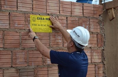 homem pregando placa de fiscalização do CREA em muro de obra