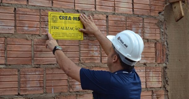 homem pregando placa de fiscalização do CREA em muro de obra