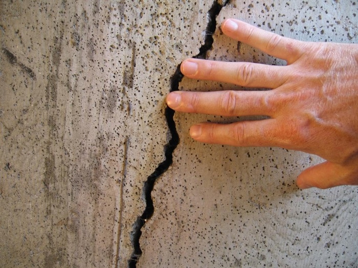 parede de concreto com uma mão sobre uma rachadura