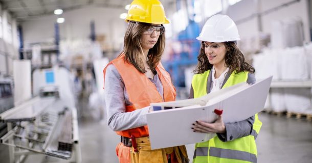 Quais são as áreas promissoras na engenharia? Duas engenherias com EPI's em pátio de produção industrial.