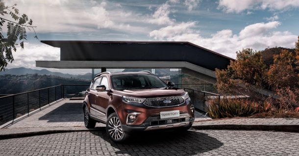 Novo Ford Territory na frente. Atrás uma casa moderna e o céu ensolarado e com nuvens