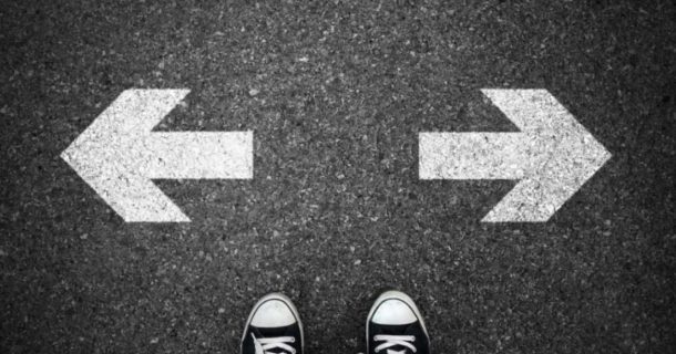 Calçados parados em frente a duas sextas, uma indicando para direita e outra para a esquerda, simbolizando uma tomada de decisão.