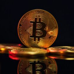 A engenharia por trás do Bitcoin: como funciona a rede que nunca parou Moeda de criptomoeda dourada em superfície escura, representando a engenharia por trás do Bitcoin.